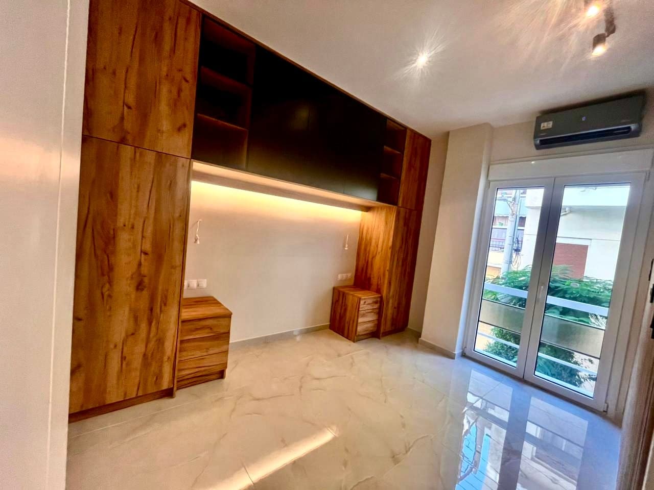 The same bedroom after renovation with fitted oak-effect wardrobes, integrated lighting and stone-effect floor