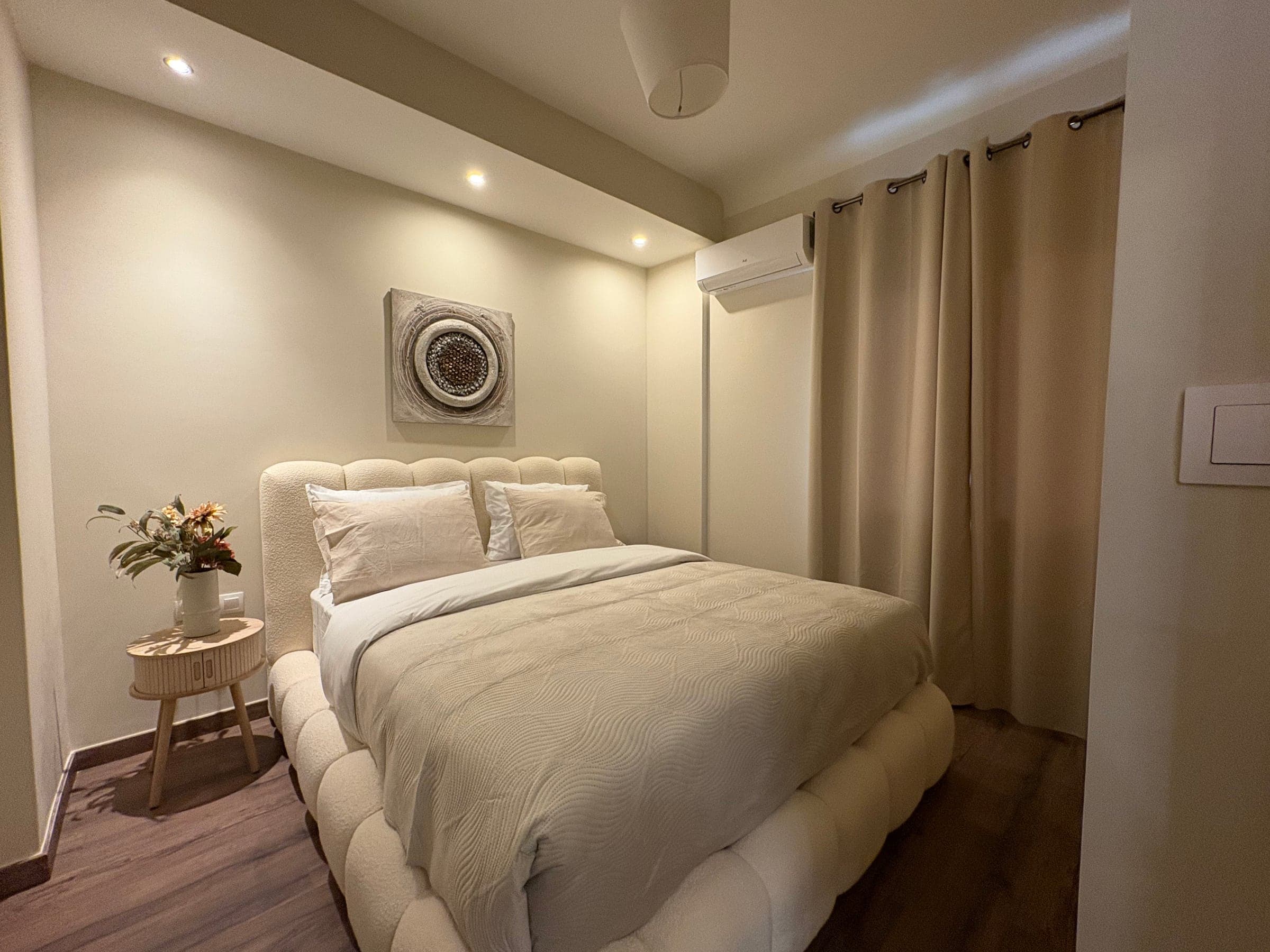 Bedroom after renovation with neutral walls, recessed spotlights and new flooring