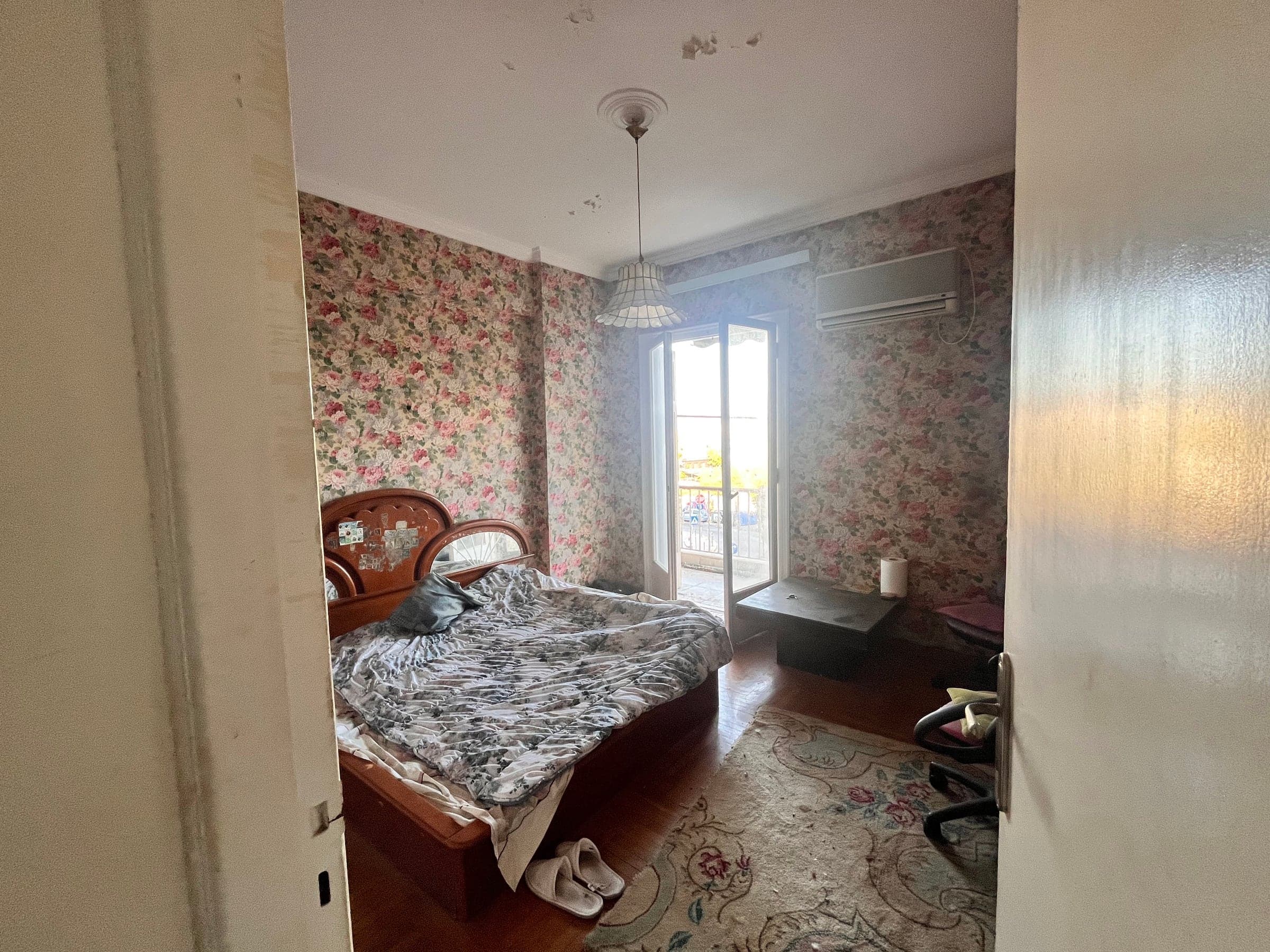 Bedroom before renovation with floral wallpaper and worn timber floor