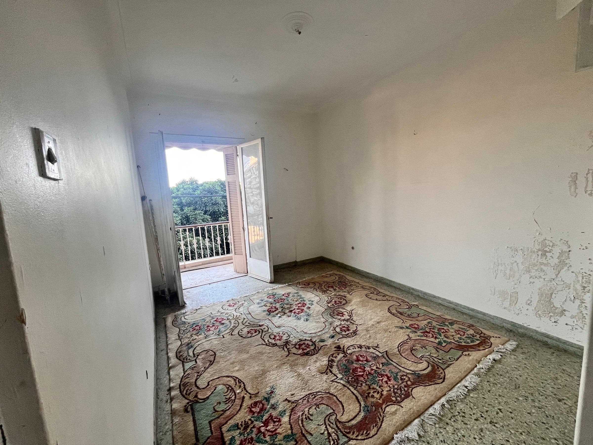 Empty room before renovation with peeling paint and a balcony door