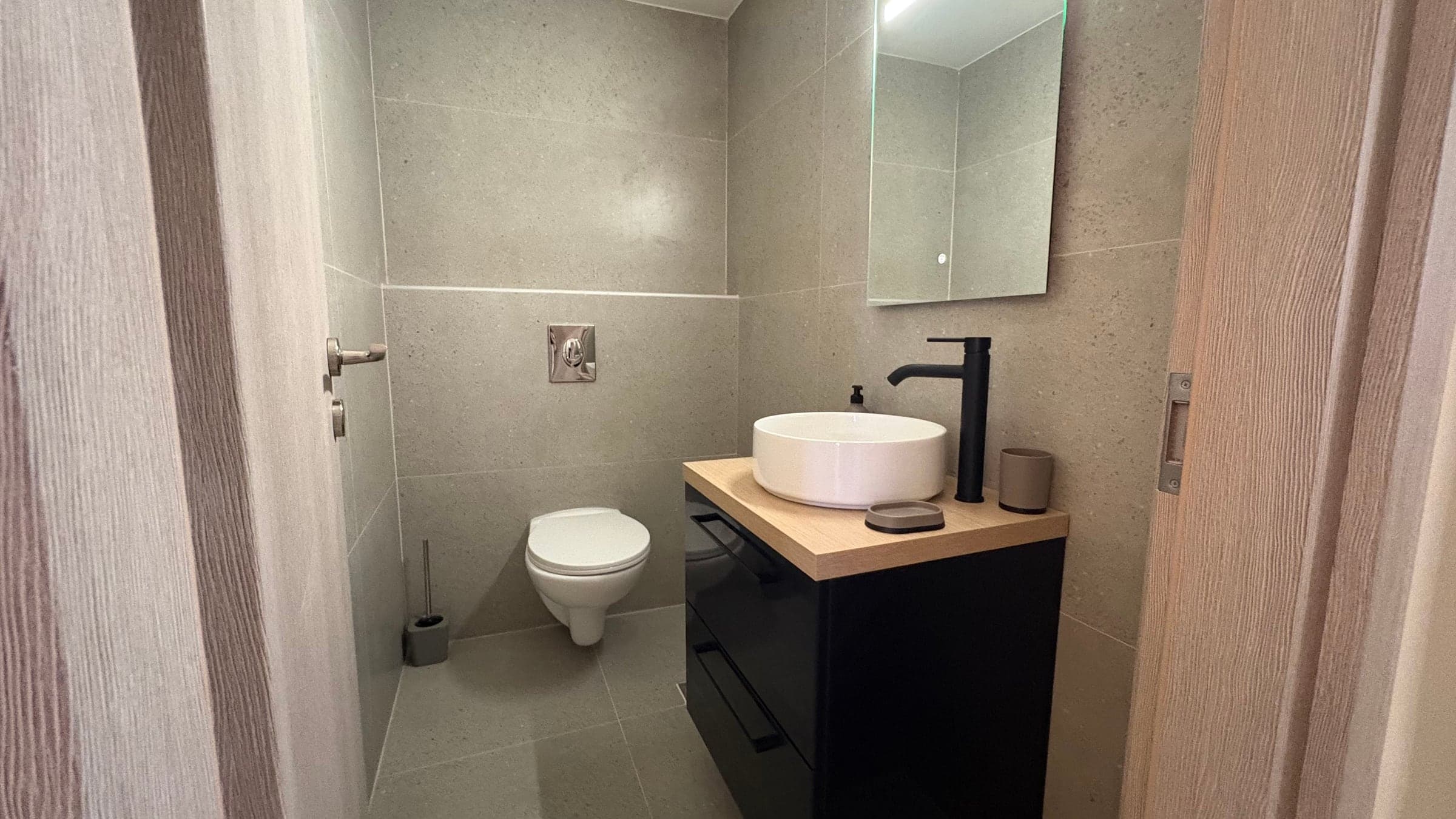 WC after renovation with large-format grey tiles, wall-hung toilet and black tap