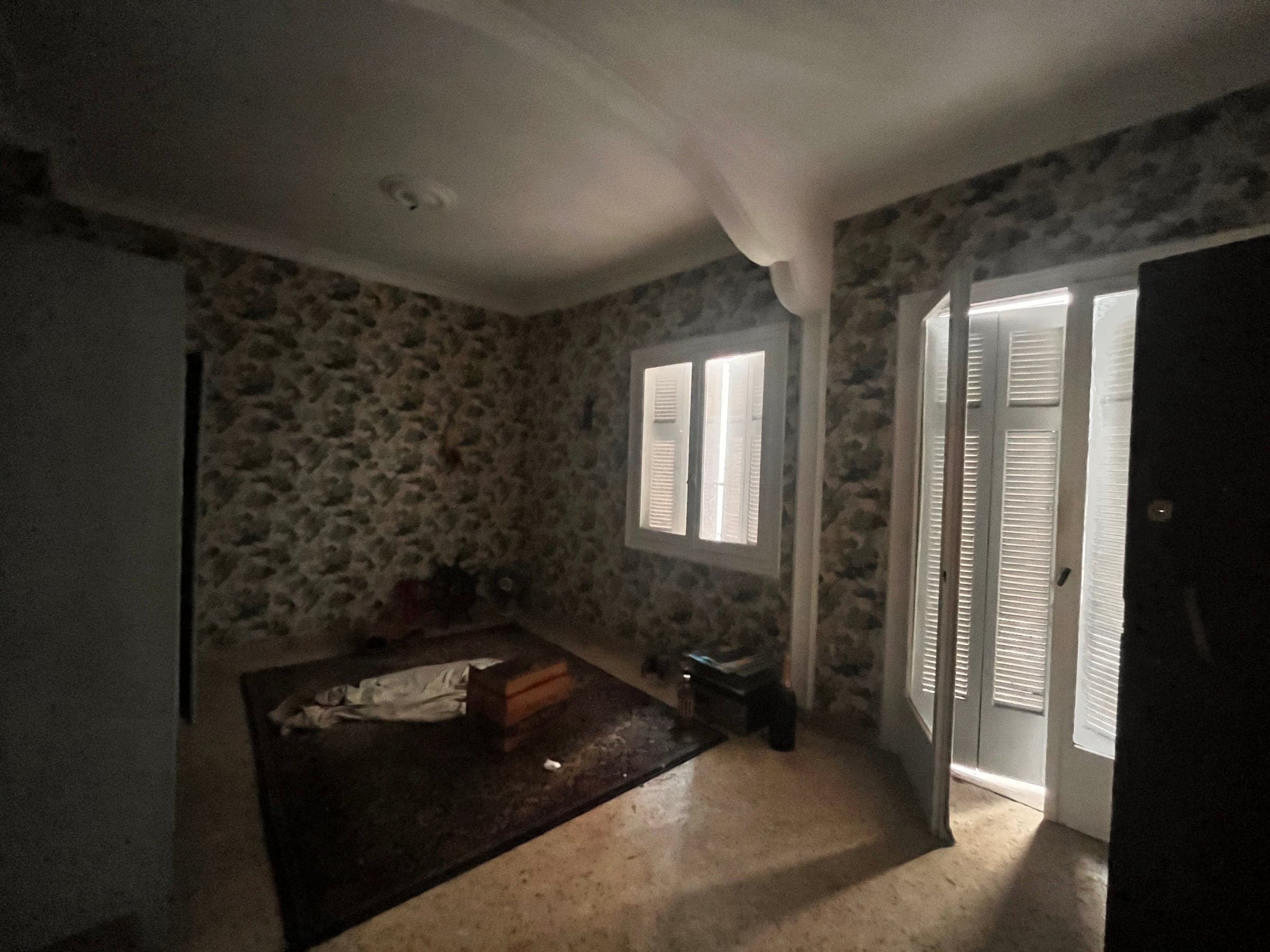 Living room before renovation: patterned wallpaper, mosaic floor, window and louvred balcony door
